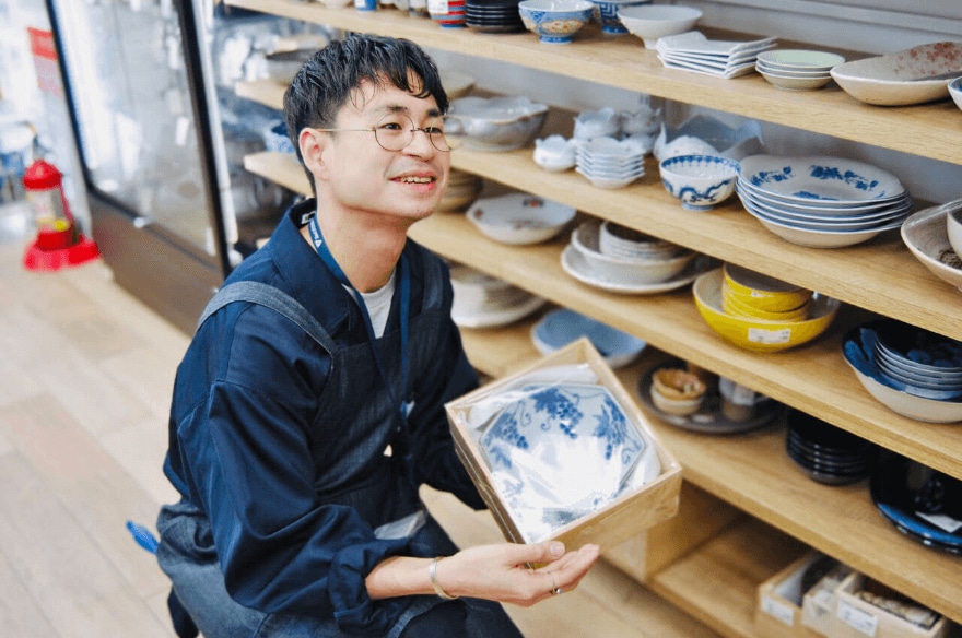 箱入りの食器を紹介する男性店員