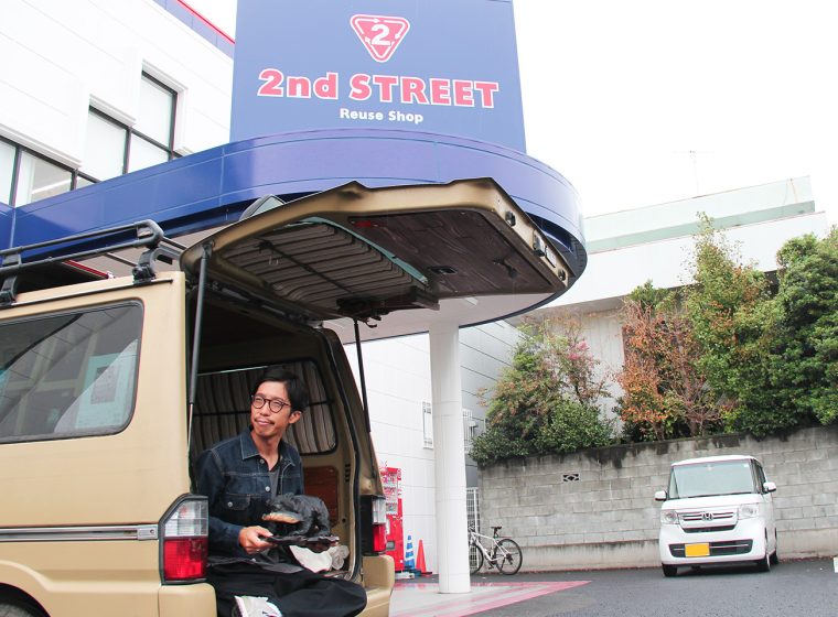 店舗をバックに自身の愛車と共に購入品をもつヘンミさん