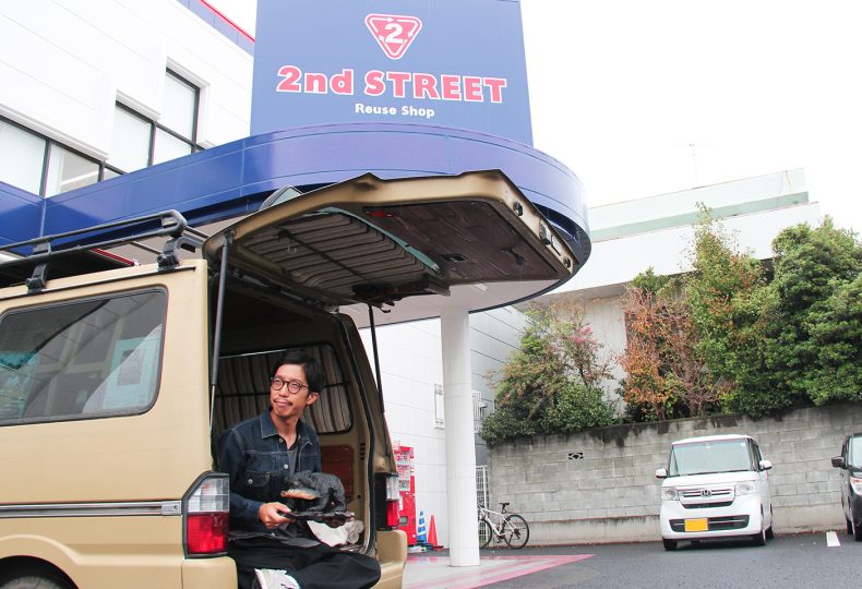 店舗をバックに自身の愛車と共に購入品をもつヘンミさん